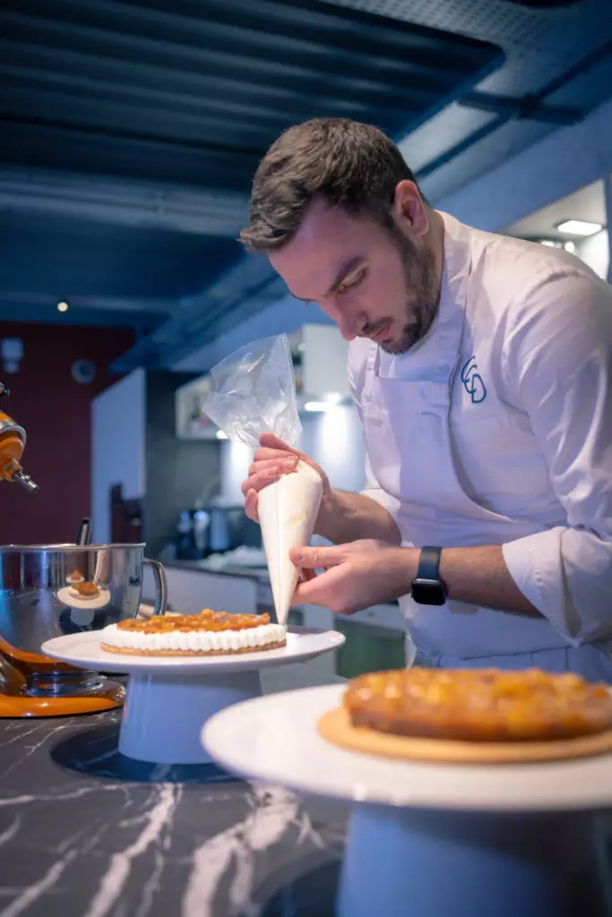 Chef pâtissier Salt & Pepper en veste blanche dresse un dessert lors d'un atelier cuisine dans une cuisine moderne.