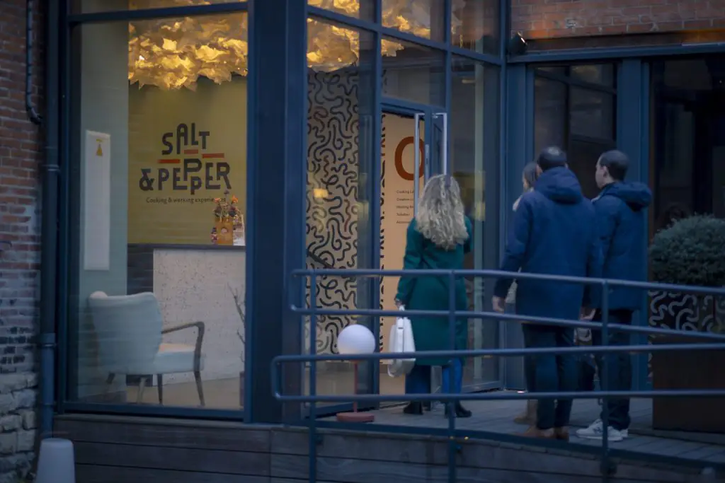 Quatre personnes entrent chez Salt & Pepper Dijon, grandes baies vitrées, déco moderne et espace pour cours de cuisine.