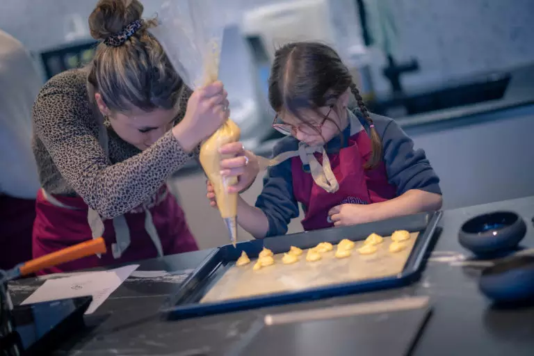 Adulte et enfant en tablier dressent de la pâte sur plaque lors d'un atelier pâtisserie chez Salt & Pepper Dijon.