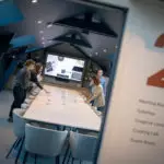 Cinq personnes en réunion, documents à la main, écran de présentation et signalisation vers un atelier culinaire Dijon.