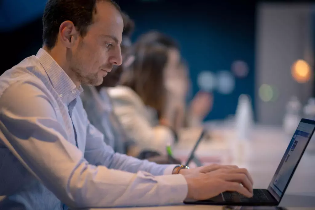 Homme en chemise claire travaillant sur ordinateur portable lors d'un séminaire à Dijon, ambiance coworking en arrière-plan.