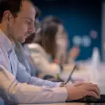 Homme en chemise claire travaillant sur ordinateur portable lors d'un séminaire à Dijon, ambiance coworking en arrière-plan.