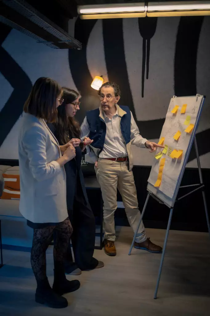 Animation team building : un homme présente des idées au paperboard devant deux collègues, décor design et lumière douce.