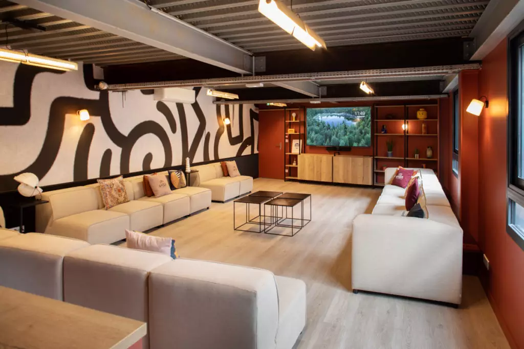 Salon spacieux avec canapés beige en U, TV, déco abstraite et ambiance chaleureuse pour ateliers ou événements d'entreprise.