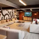 Salon spacieux avec canapés beige en U, TV, déco abstraite et ambiance chaleureuse pour ateliers ou événements d'entreprise.