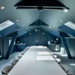 Salle séminaire Salt & Pepper Dijon, chaises grises, plafond bleu incliné, puits de lumière, kitchenette en fond.