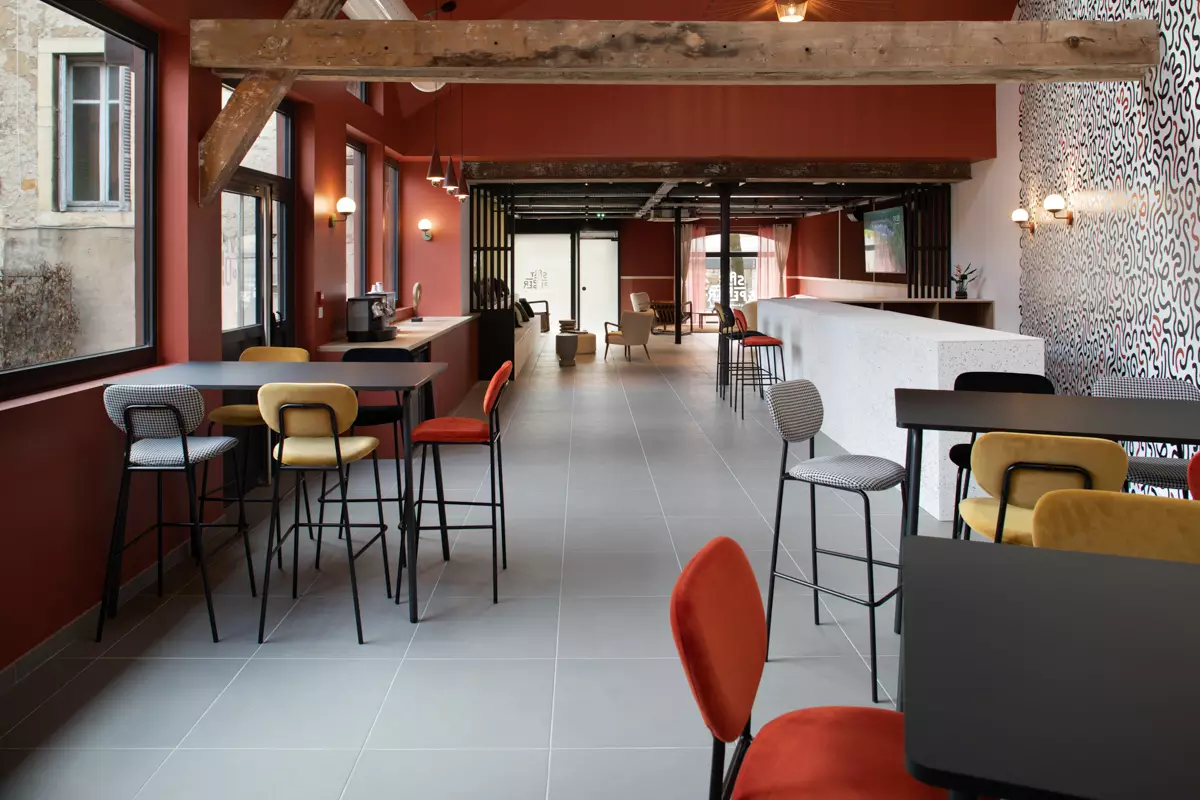 Café moderne aux murs rouges, tables noires et chaises colorées, idéal pour atelier culinaire ou événement d'entreprise.