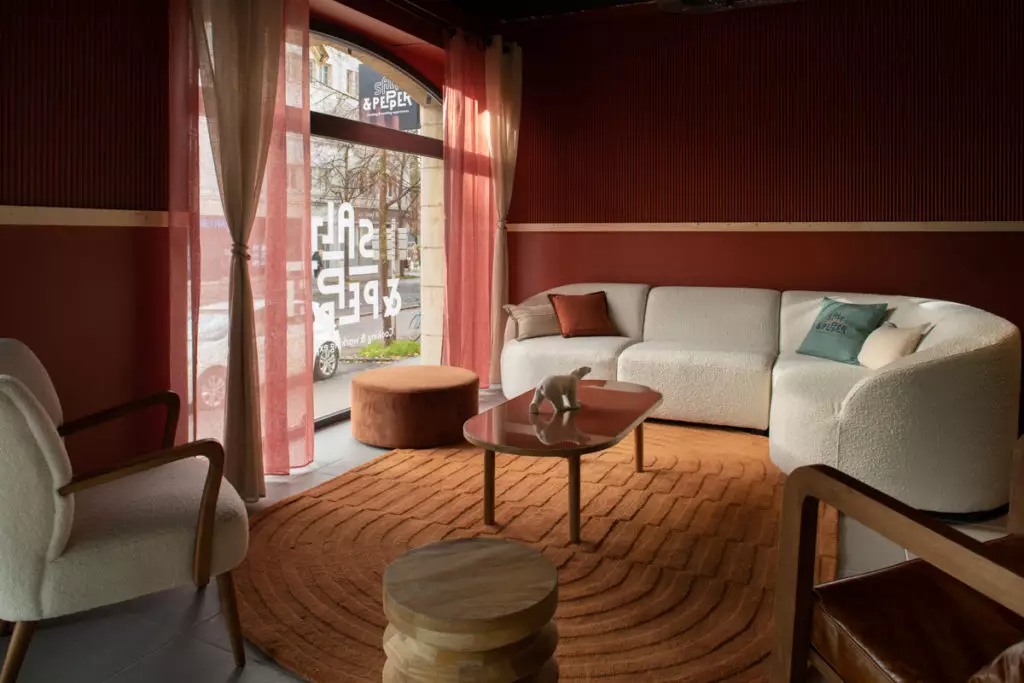 Salon chaleureux avec canapé blanc, fauteuils et ottoman sur tapis rouille, table basse décorée, lumière idéale pour team building.