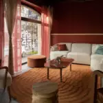 Salon chaleureux avec canapé blanc, fauteuils et ottoman sur tapis rouille, table basse décorée, lumière idéale pour team building.
