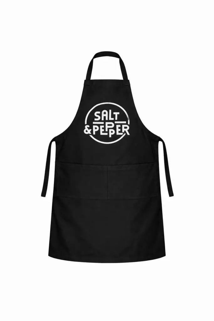 Tablier noir à poche, liens noués, inscription "SALT & PEPPER" blanche pour ateliers cuisine ou team building.