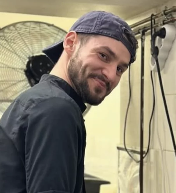 Homme barbe courte et casquette à l'envers sourit en cuisine Salt & Pepper Dijon lors d'un atelier tapas team building.